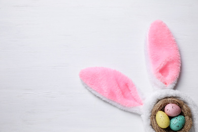 Photo of Headband with bunny ears, painted eggs and space for text on white wooden background, flat lay. Easter holiday