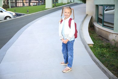 Photo of Cute little girl with backpack on city street. Space for text