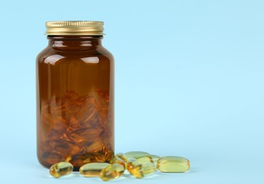 Jar with vitamin capsules on light blue background, space for text