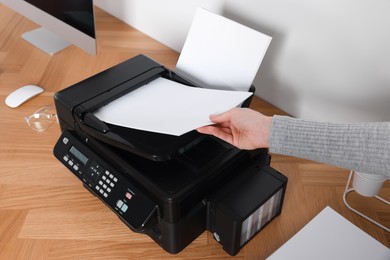 Woman loading paper into printer at wooden table indoors, closeup