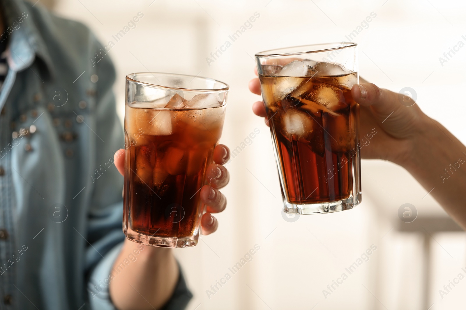 Photo of Women holding glasses of cola with ice on blurred background, closeup