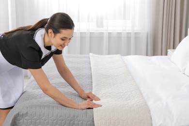 Young maid making bed in hotel room