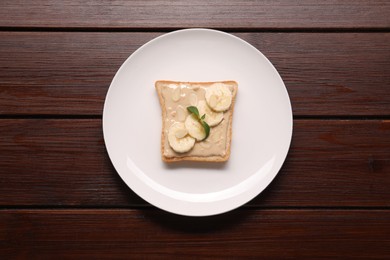 Photo of Toast with tasty nut butter, banana slices and almond flakes on wooden table, top view