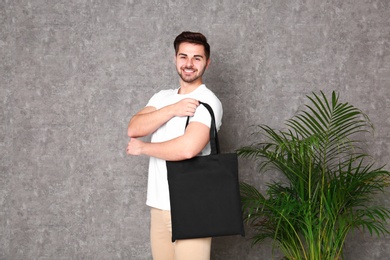 Portrait of young man with eco bag at indoor palm plant near grey wall