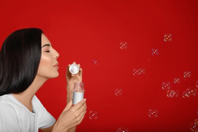 Young woman blowing soap bubbles on red background, space for text