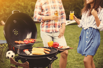 Image of People with beverages near barbecue grill outdoors on sunny day