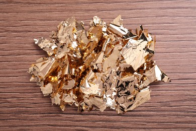 Photo of Many pieces of edible gold leaf on wooden table, top view