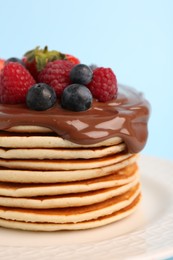Photo of Stack of tasty pancakes with fresh berries and chocolate spread on light blue background, closeup