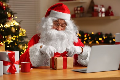 Photo of Santa Claus decorating Christmas gift with ribbon at home