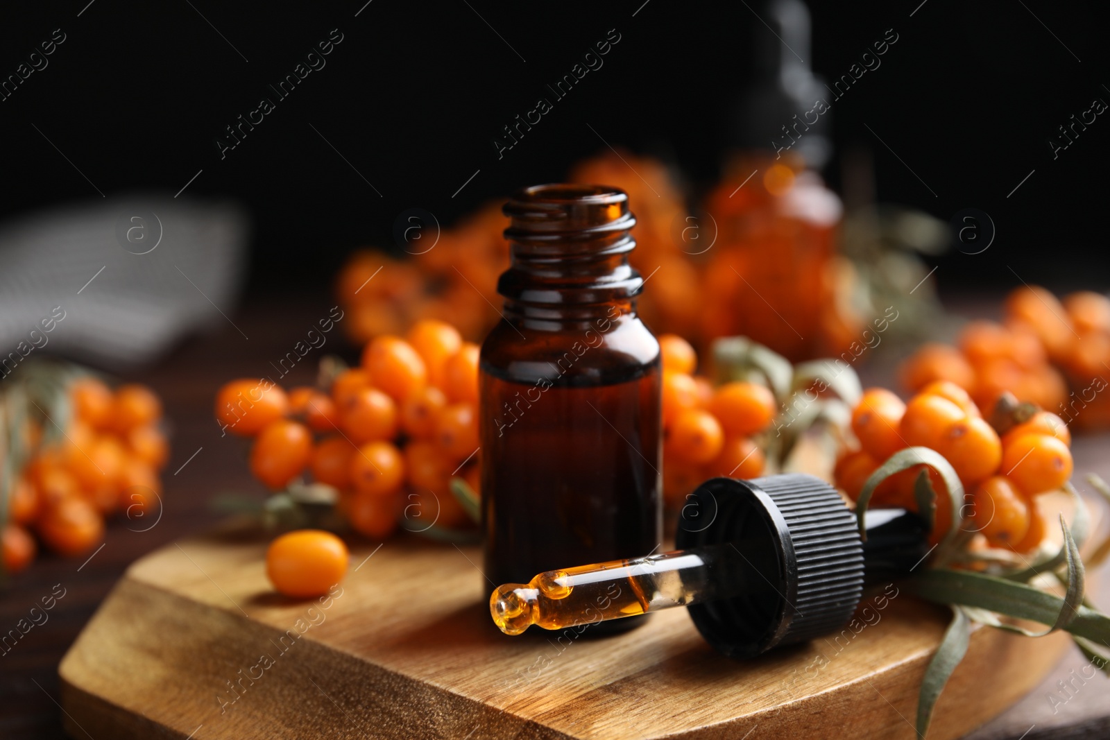 Photo of Ripe sea buckthorn and essential oil on wooden board against black background