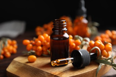 Photo of Ripe sea buckthorn and essential oil on wooden board against black background