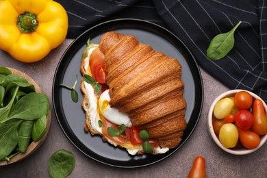 Photo of Tasty croissant with fried egg, tomato and microgreens on brown textured table, flat lay
