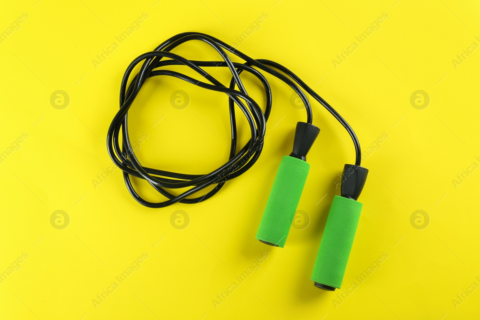 Photo of Skipping rope on yellow background, top view. Sports equipment