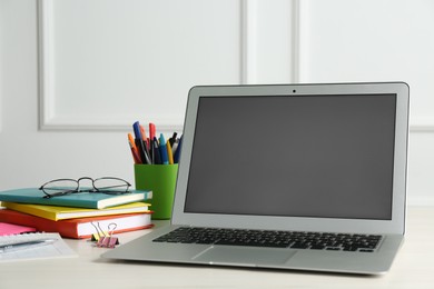 Photo of Modern laptop and office supplies on wooden table indoors. Distance learning