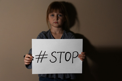 Abused little girl with hashtag STOP near beige wall. Domestic violence concept