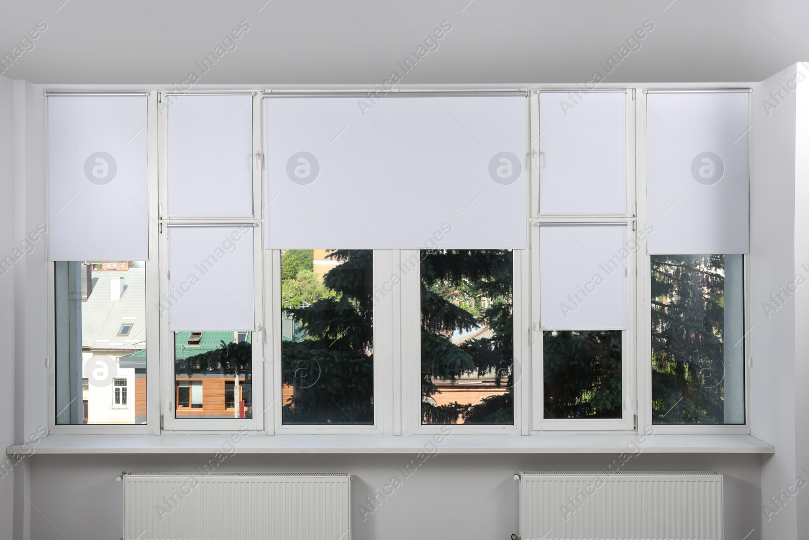 Photo of Large window with white roller blinds indoors