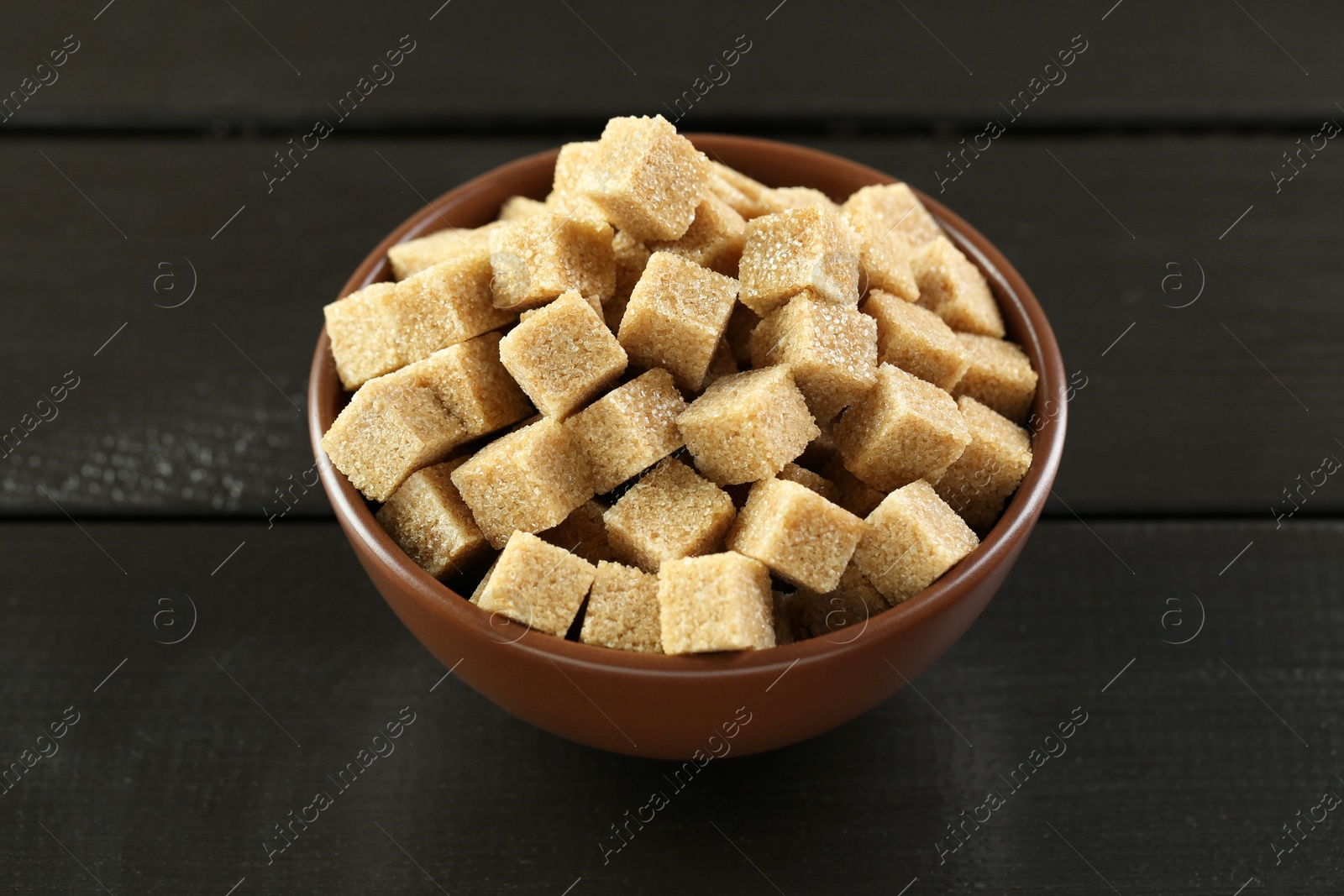 Photo of Brown sugar cubes in bowl on black wooden table, closeup