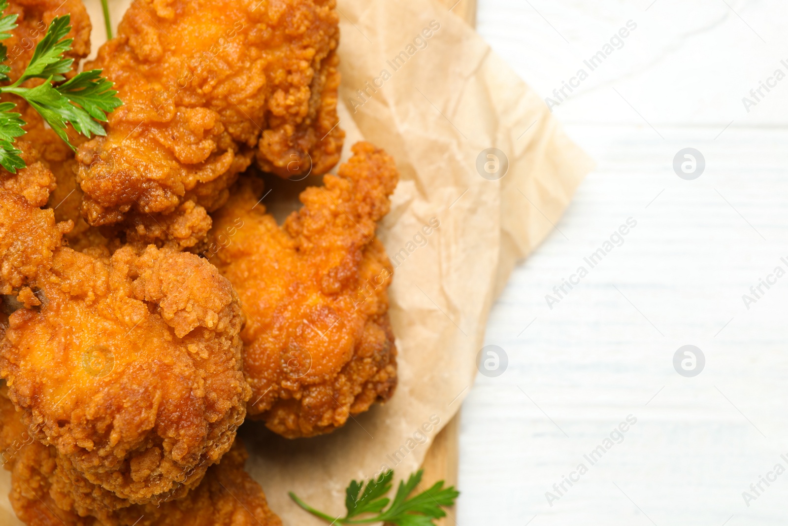 Photo of Tasty deep fried chicken pieces on white wooden table, top view. Space for text