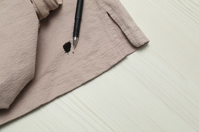 Photo of Clothes with stain of black ink and pen on wooden table, top view. Space for text