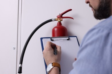 Photo of Man with clipboard checking fire extinguisher indoors, closeup