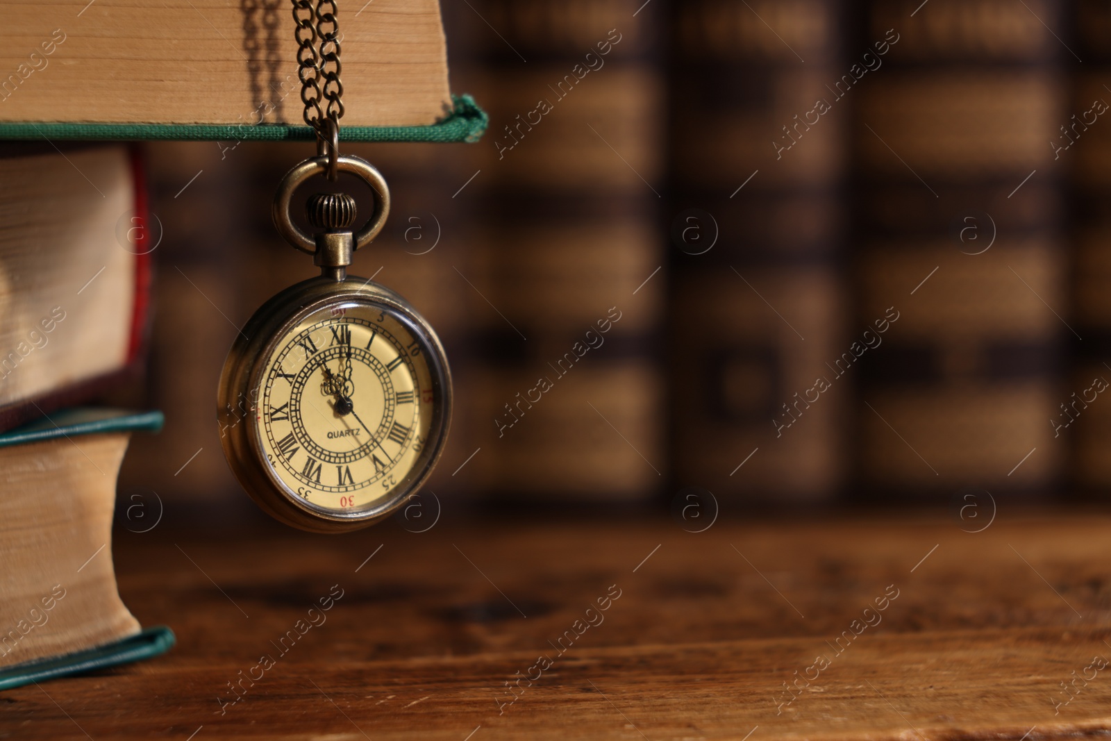 Photo of Pocket clock hanging on stack of books at wooden table, closeup. Space for text