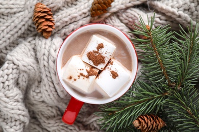 Photo of Cup of tasty cocoa with marshmallows on knitted cloth, flat lay