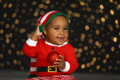 Cute little African American baby with Christmas ball and blurred lights on dark background