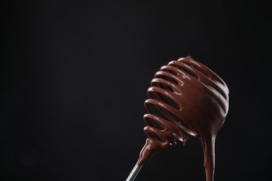 Chocolate cream flowing from whisk on black background, closeup. Space for text