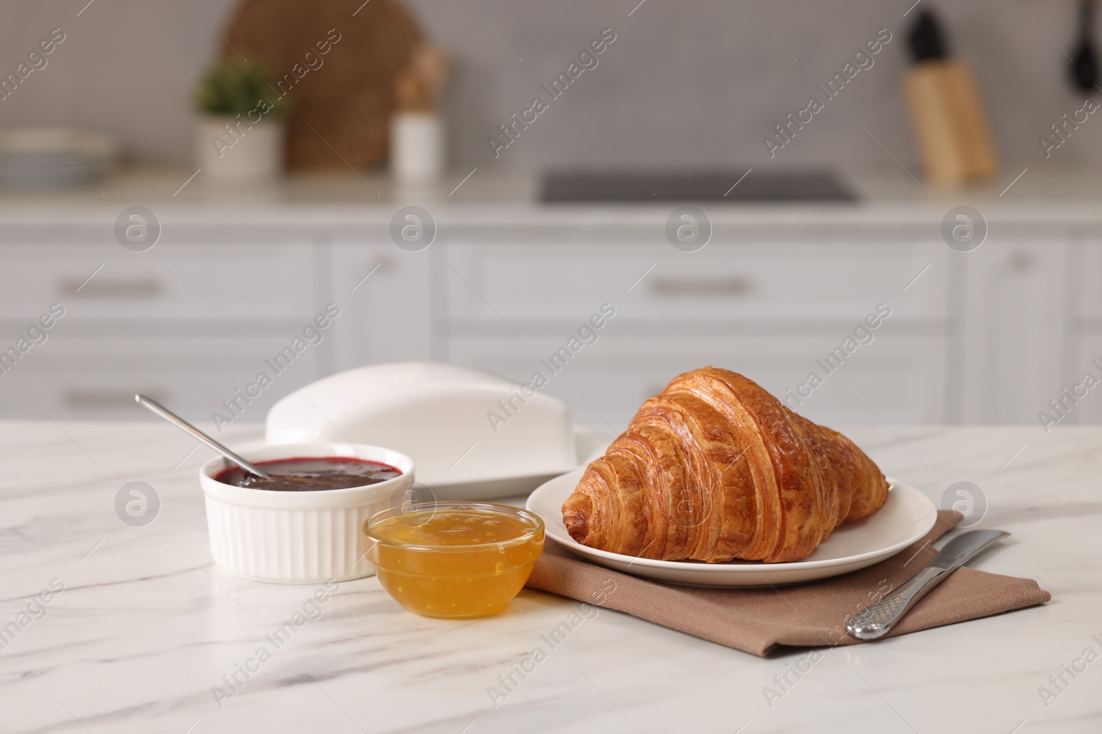 Photo of Breakfast served in kitchen. Fresh croissant, jam and honey on white table