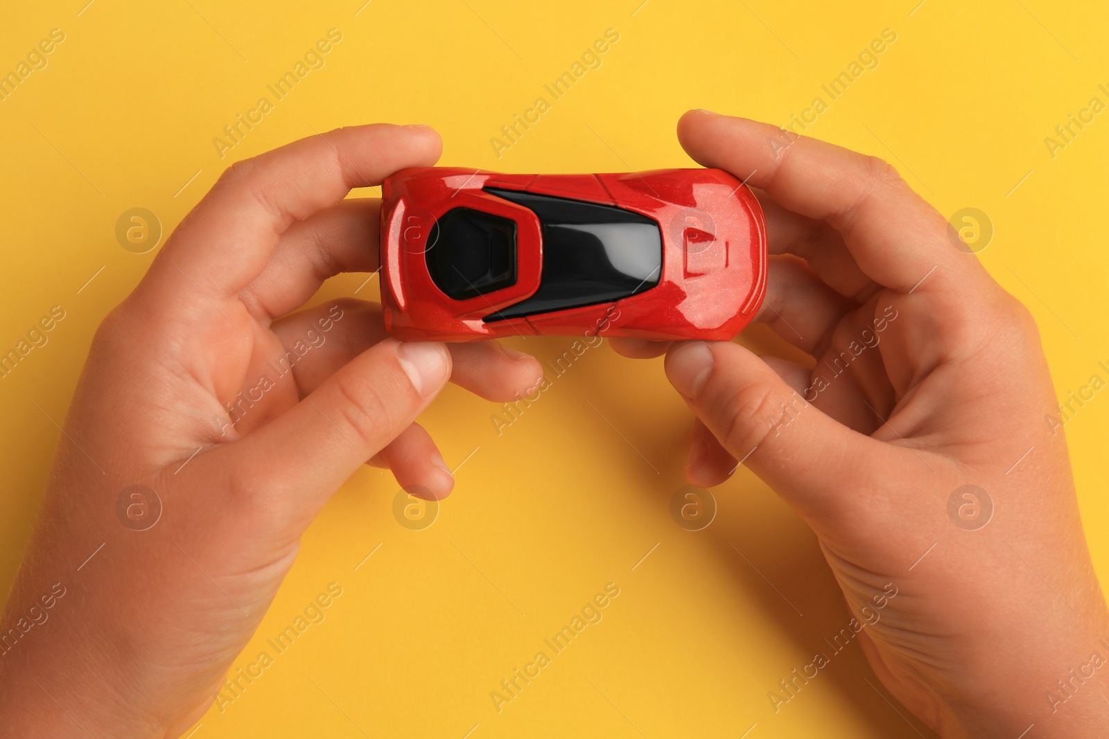 Photo of Child holding toy car on yellow background, top view