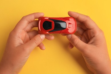 Photo of Child holding toy car on yellow background, top view