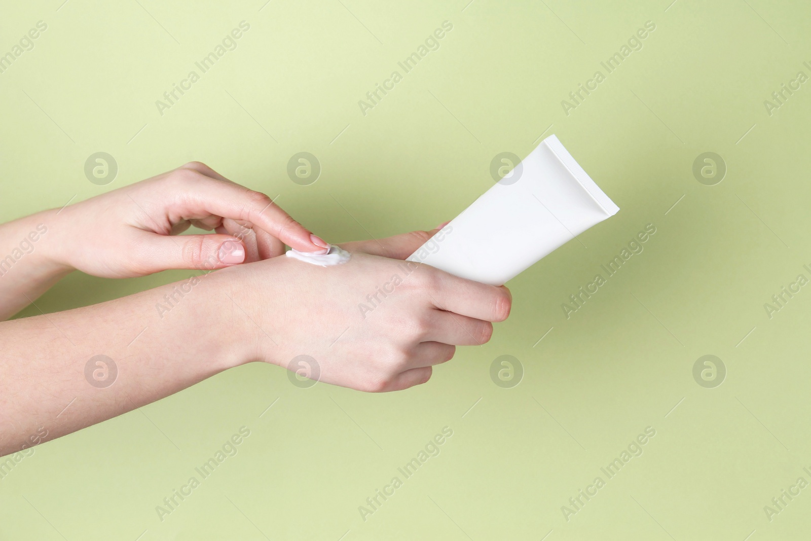 Photo of Woman with tube applying cream on her hand against green background, closeup