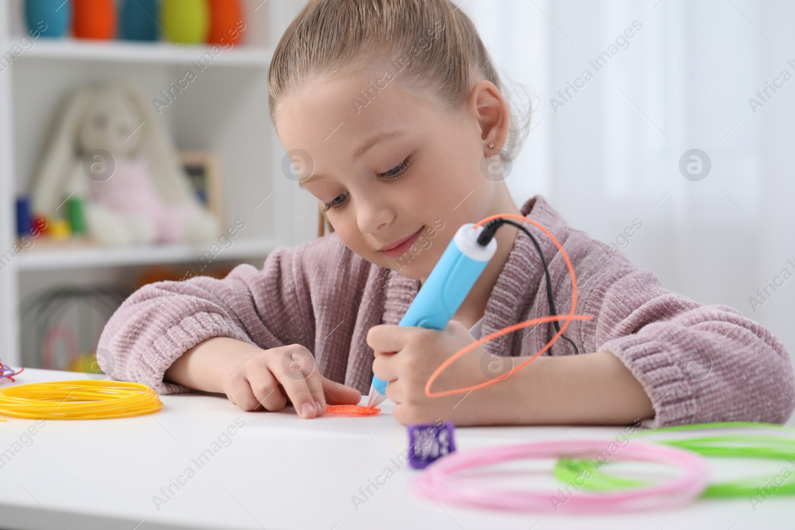 Photo of Girl drawing with stylish 3D pen at white table indoors