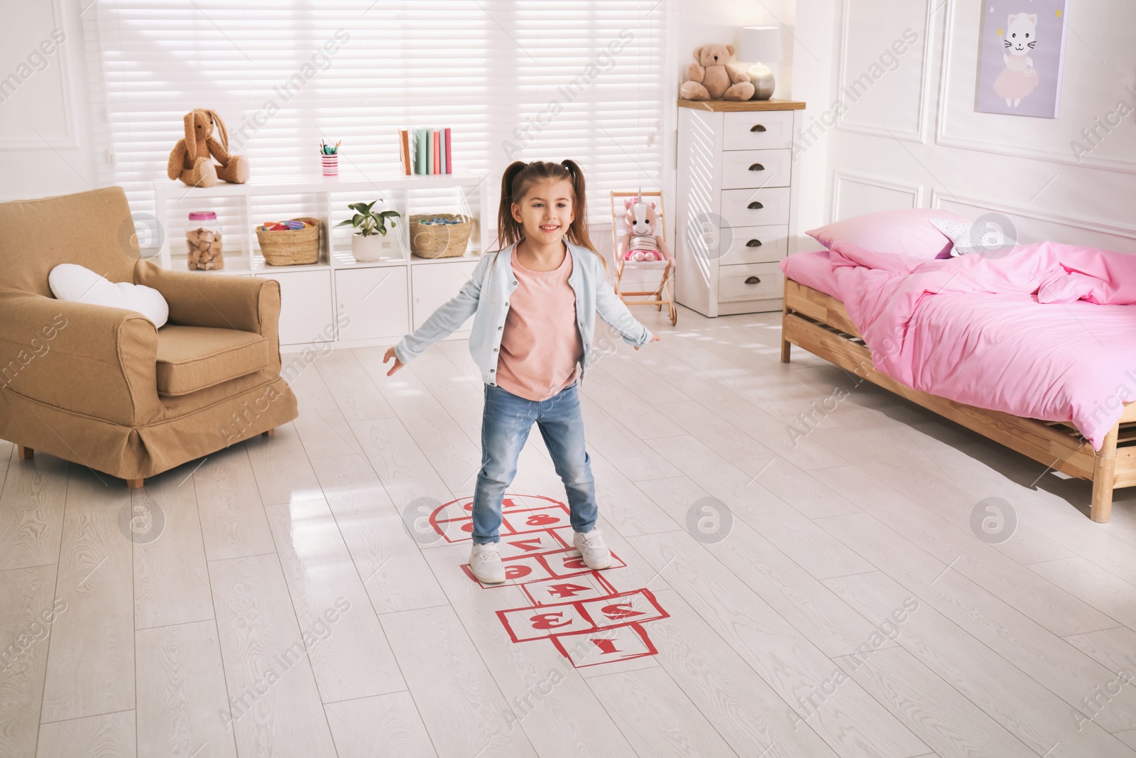 Photo of Cute little girl playing hopscotch at home