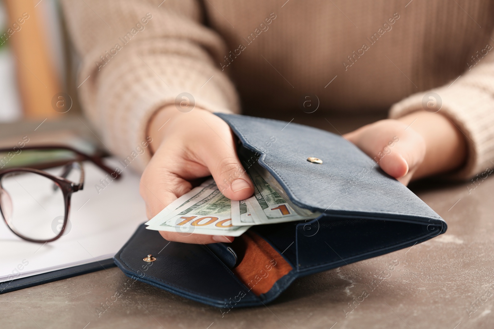 Photo of Woman putting money into wallet at brown table, closeup