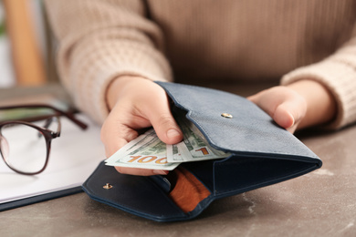 Photo of Woman putting money into wallet at brown table, closeup