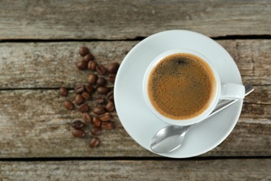 Photo of Cup of tasty coffee and beans on wooden table, flat lay