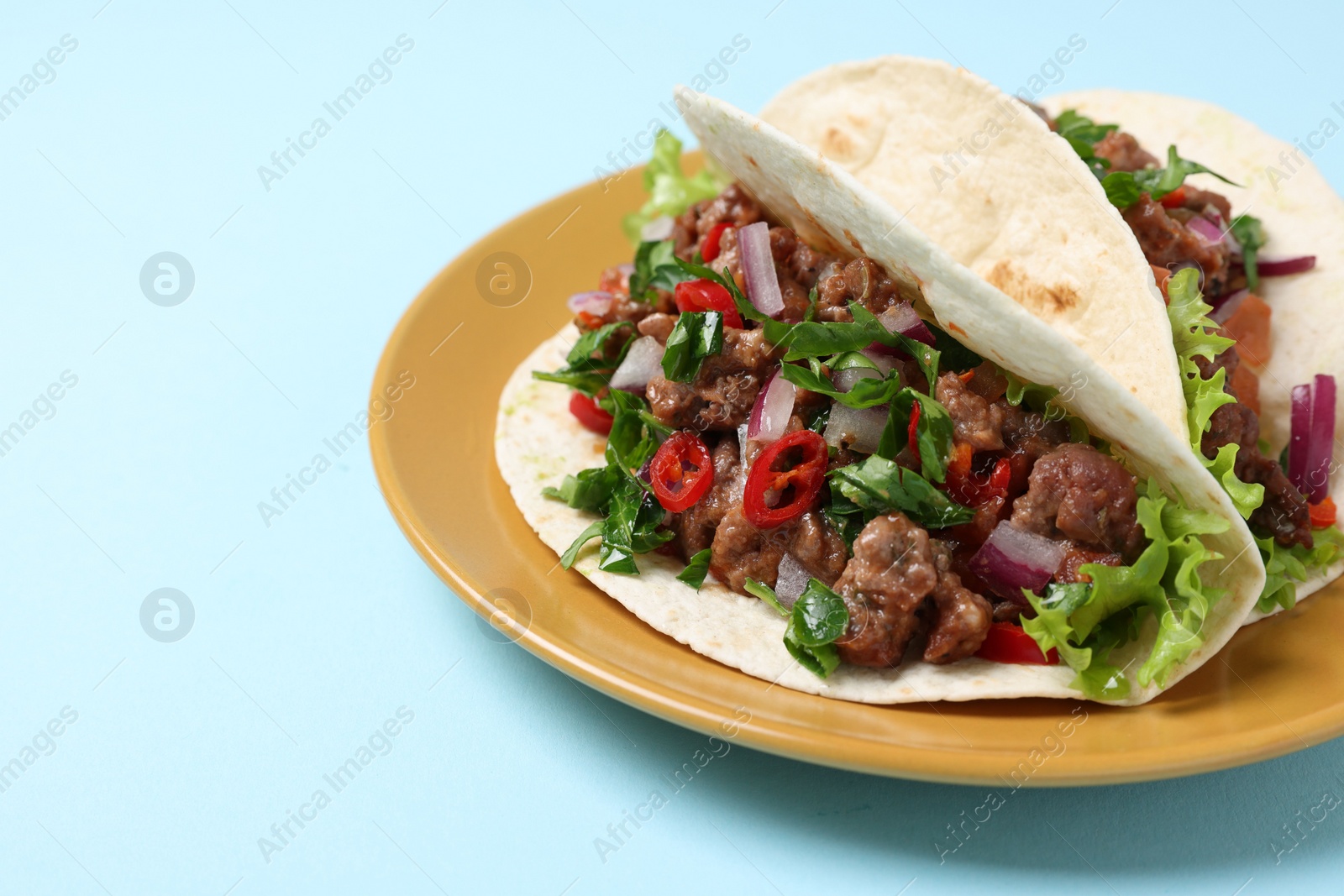 Photo of Delicious tacos with meat and vegetables on light blue table, closeup