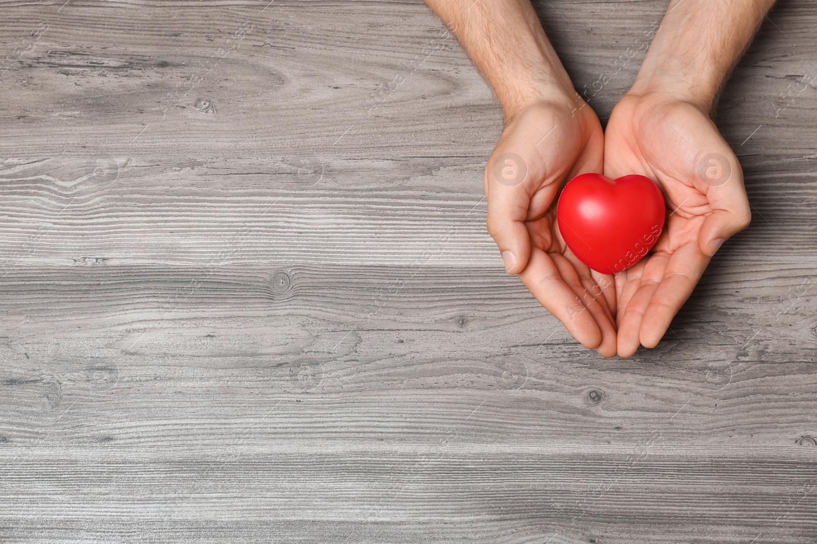 Photo of Young man holding red heart on grey wooden background, top view with space for text. Donation concept