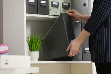 Woman taking folder from shelf in office, closeup