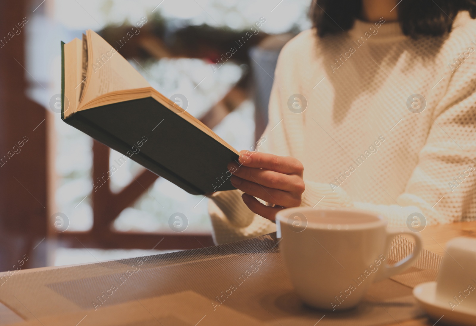 Image of Woman with coffee reading book at wooden table, closeup