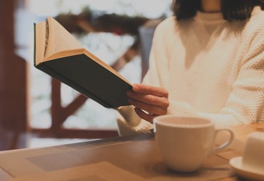 Image of Woman with coffee reading book at wooden table, closeup