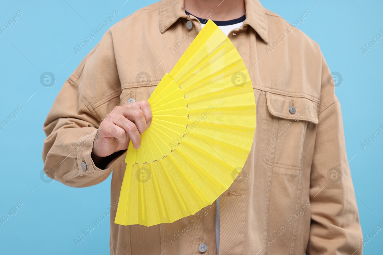 Photo of Man holding hand fan on light blue background, closeup