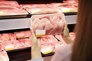 Photo of Woman choosing packed chicken meat in supermarket