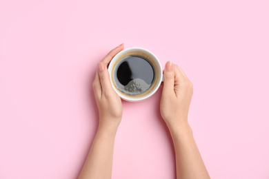 Photo of Woman with cup of coffee on light pink background, top view