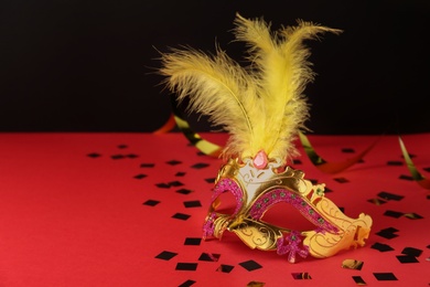 Photo of Beautiful golden carnival mask and shiny confetti on red table. Space for text