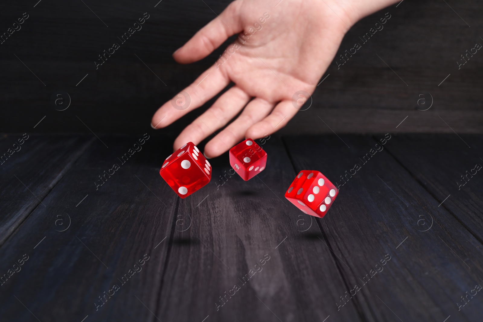 Image of Woman throwing red dice on black wooden table, closeup
