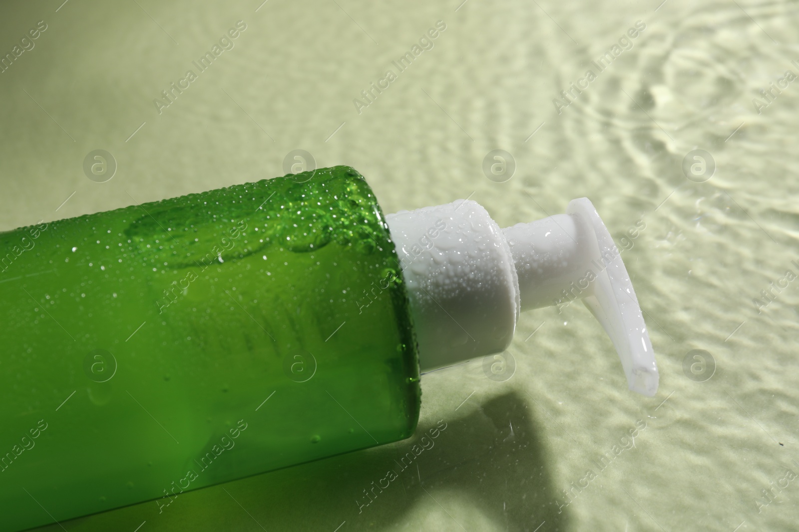 Photo of Bottle of facial cleanser in water against olive background, closeup
