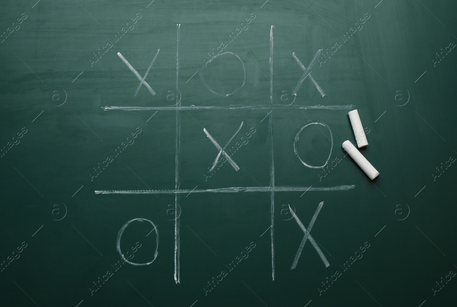 Photo of Tic tac toe game and pieces of chalk on greenboard, flat lay