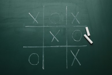 Photo of Tic tac toe game and pieces of chalk on greenboard, flat lay